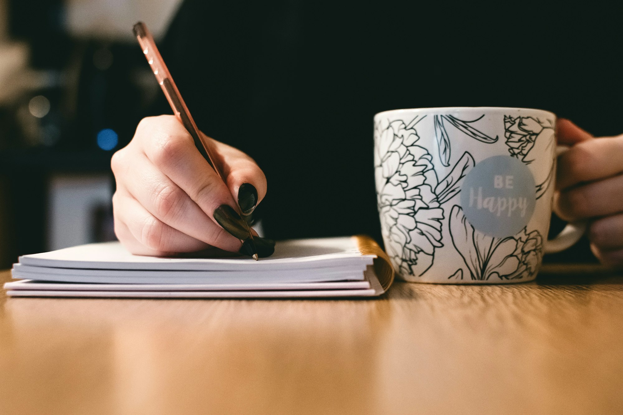 a cup and a person writing on a paper tablet with a pen