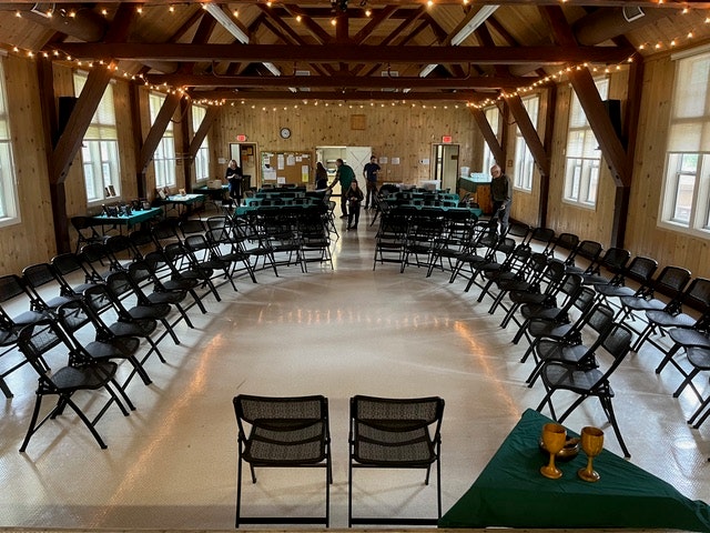 Wooden hall with chairs arranged in circles, string lights above, and people in the background.