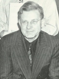 A black and white photo of a man wearing glasses and a suit.