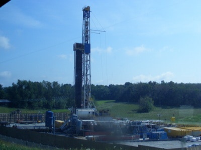 An oil drilling rig set up in a grassy field under a clear blue sky.