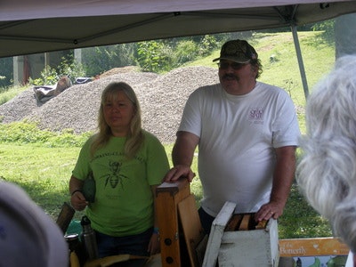 Two people standing under a canopy at an outdoor event, surrounded by beekeeping equipment.