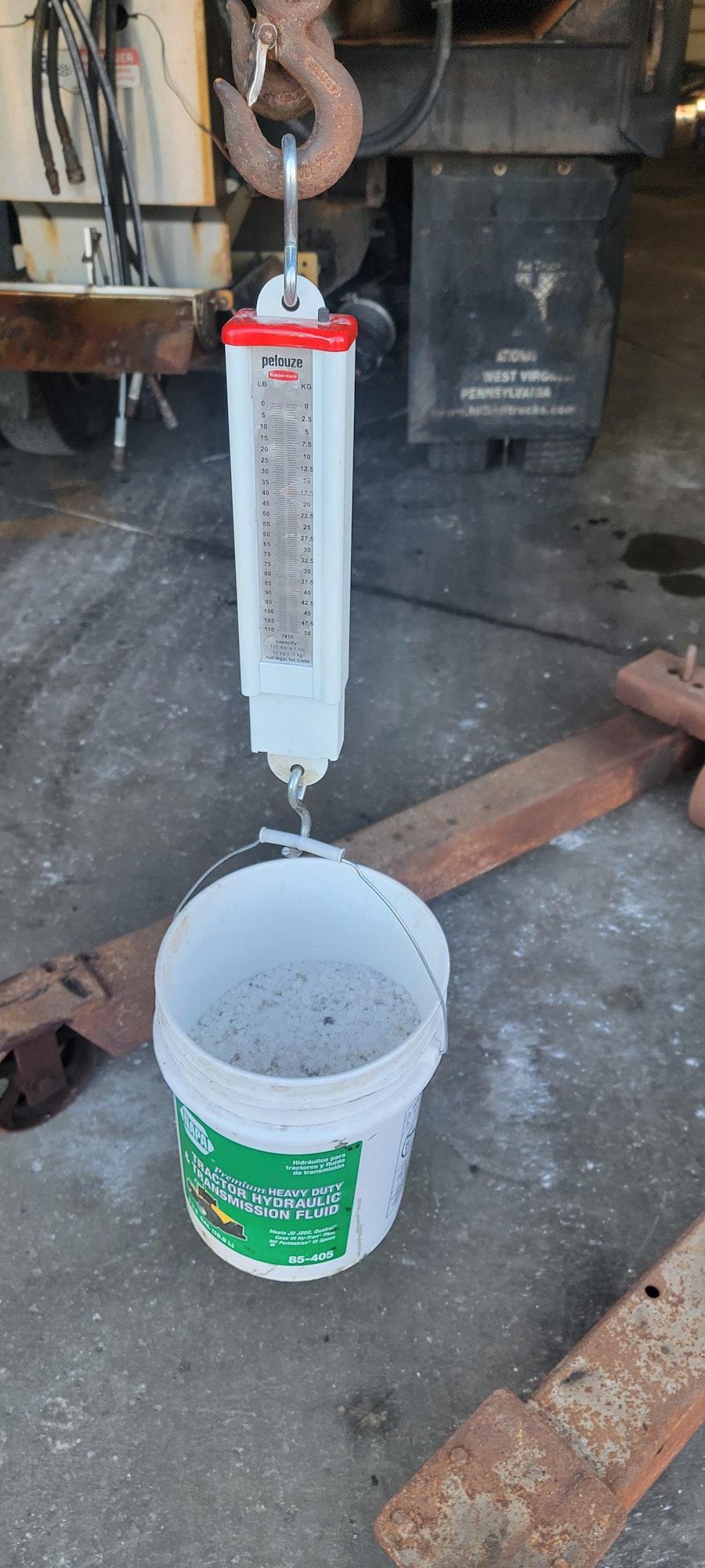 The image shows a weighing scale attached to a hook with a bucket underneath it, likely used for measuring weight.