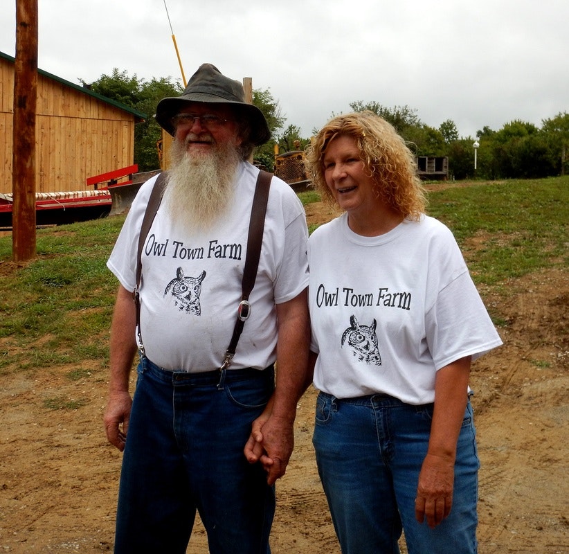 Two people wearing "Owl Town Farm" shirts holding hands outside, with a barn in the background.