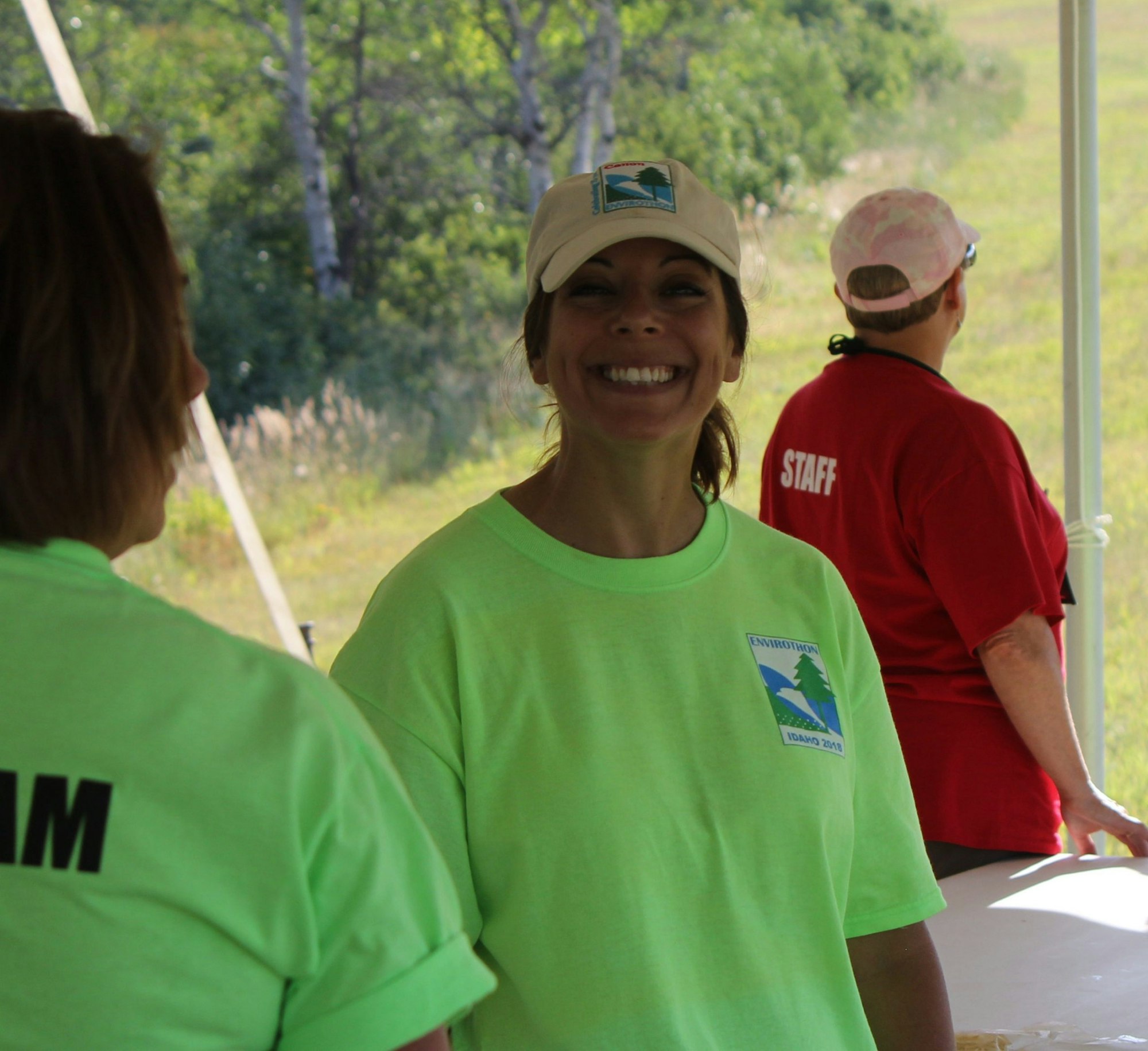 Three people in bright shirts at an outdoor event, one smiling.