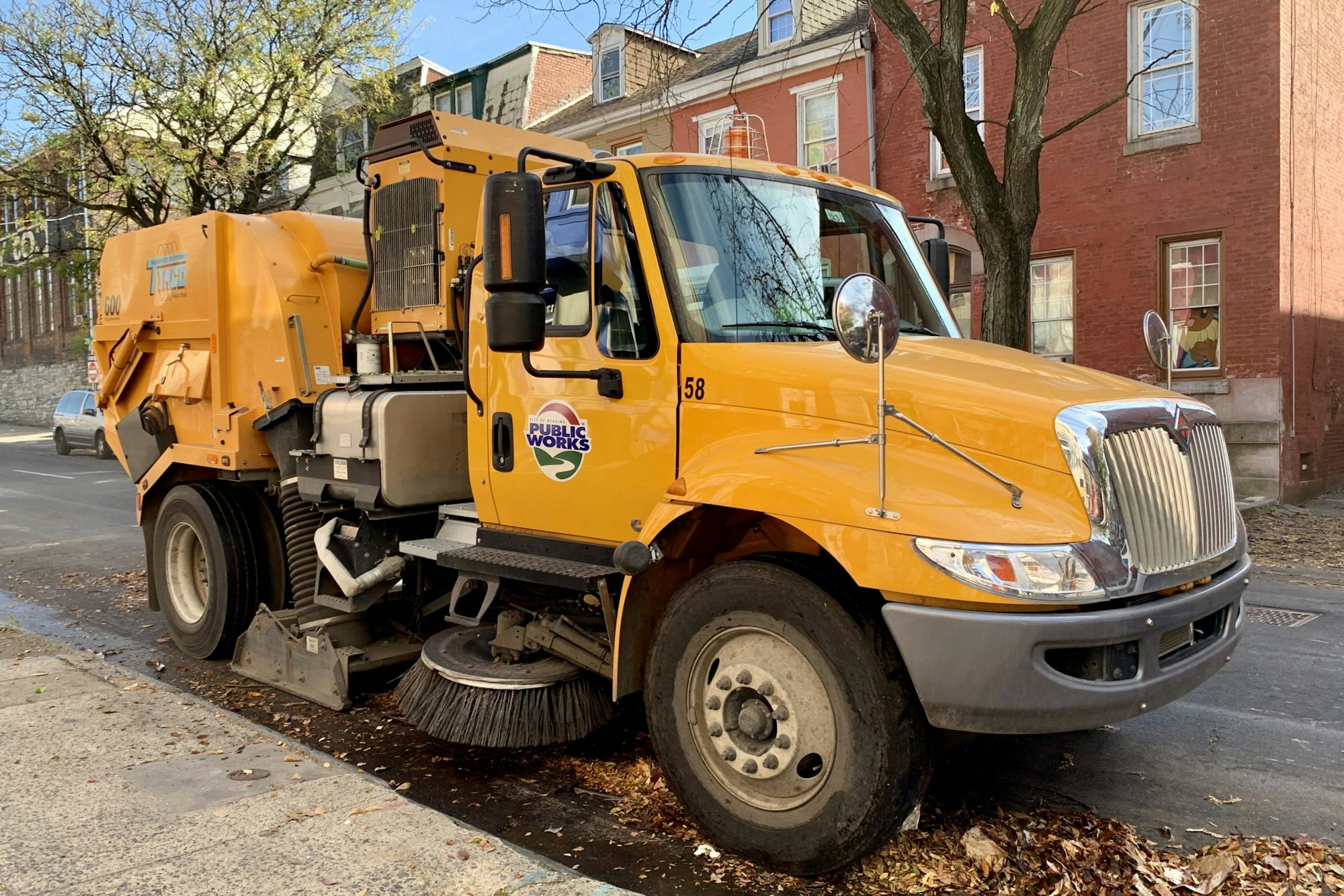 A yellow street sweeper truck parked on a residential street, labeled "Public Works."
