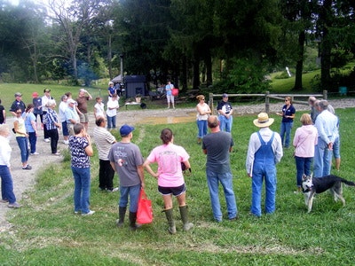 A group of people gathered in a circle on grass, listening to a speaker.