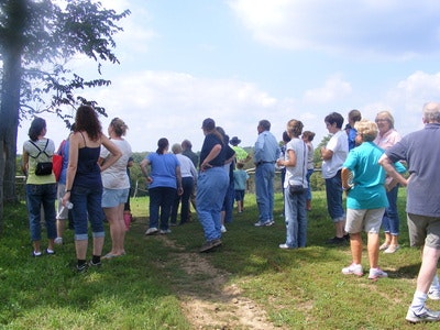 A group of people standing outdoors on a grassy area under a partly cloudy sky.