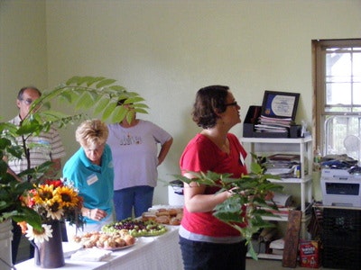 People in a room with a table of snacks and flowers.
