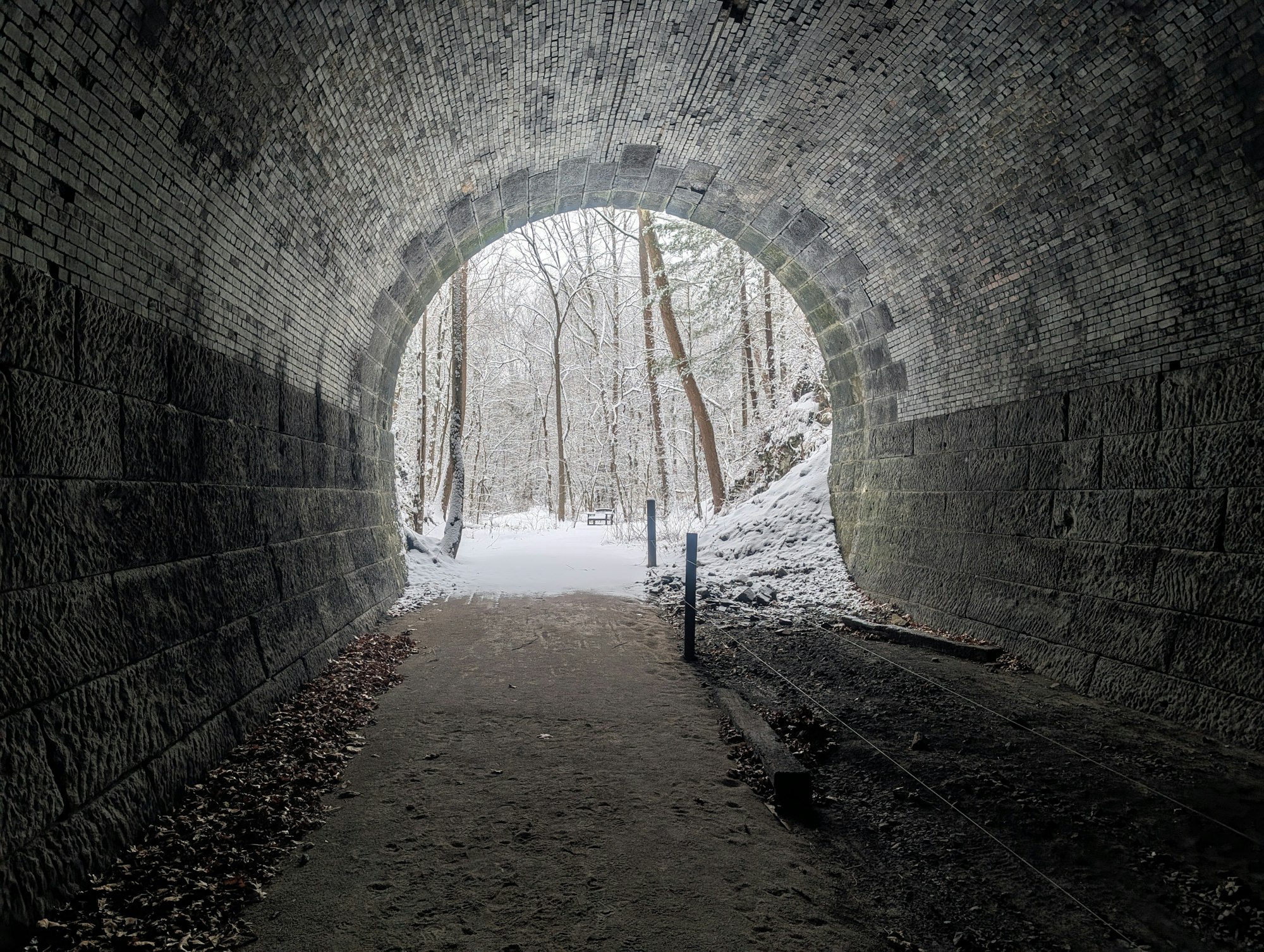 A snow-covered landscape viewed through a stone tunnel; trees are visible, hinting at a serene winter scene.