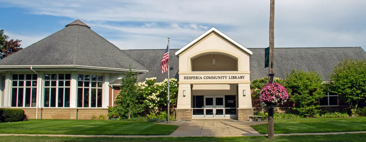 The image shows the Hesperia Community Library, featuring a modern design, greenery, and an American flag.