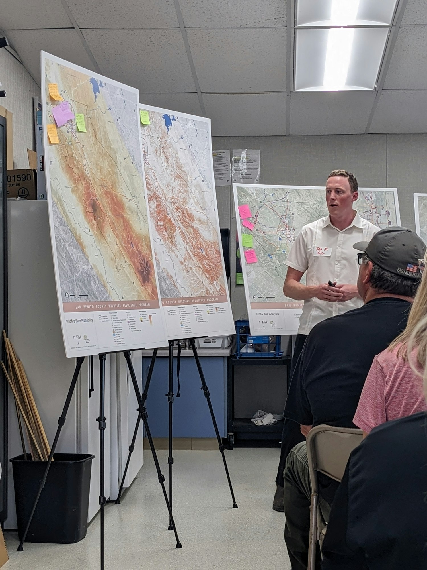 A man presents large maps on easels to an attentive audience in a room:Ian Moore, Spatial Informatics Group, explaining San Benito Wildfire Risk Assessment and Strategies