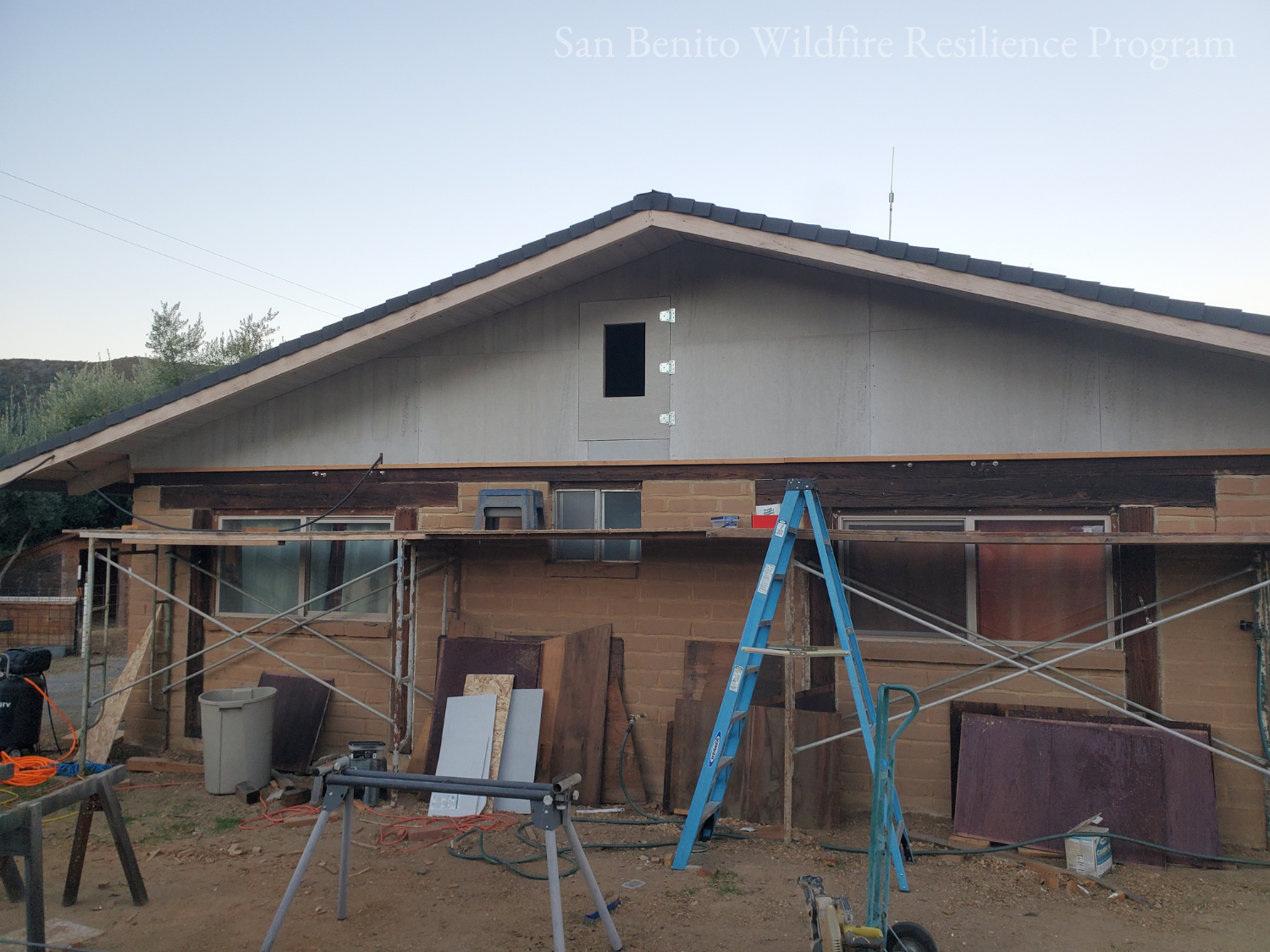 House exterior under renovation, scaffolding, tools, ladders, and construction materials present.