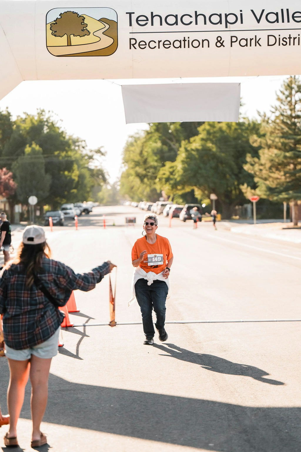 Person running a race, nearing the finish line under a Tehachapi Valley Recreation & Park District banner, greeted by a supporter.