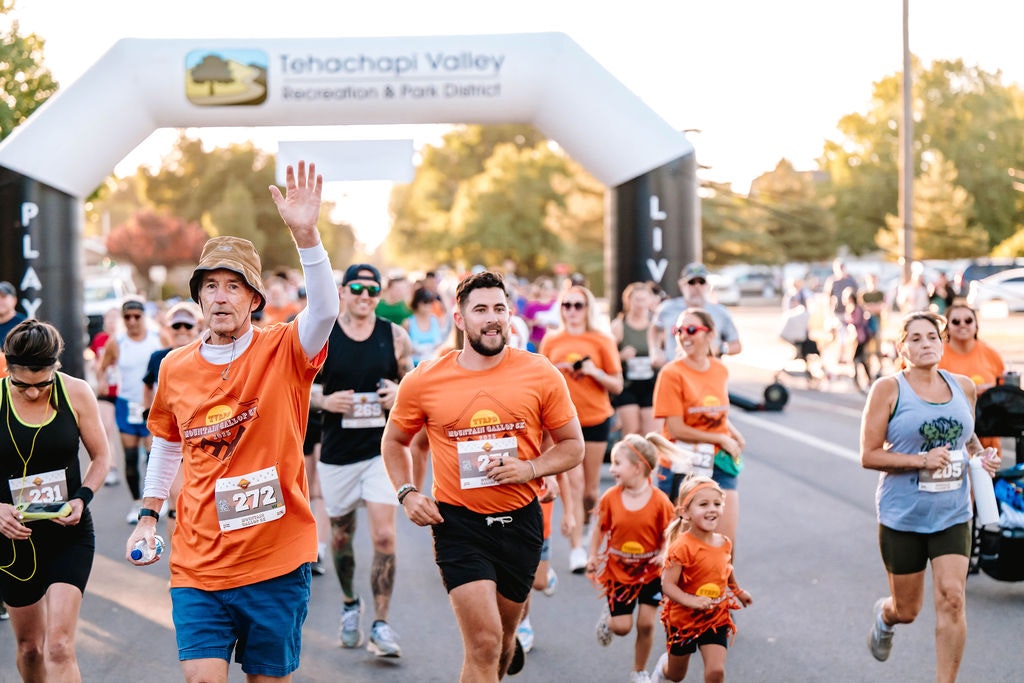 A group of people running in a race under a Tehachapi Valley Recreation arch.
