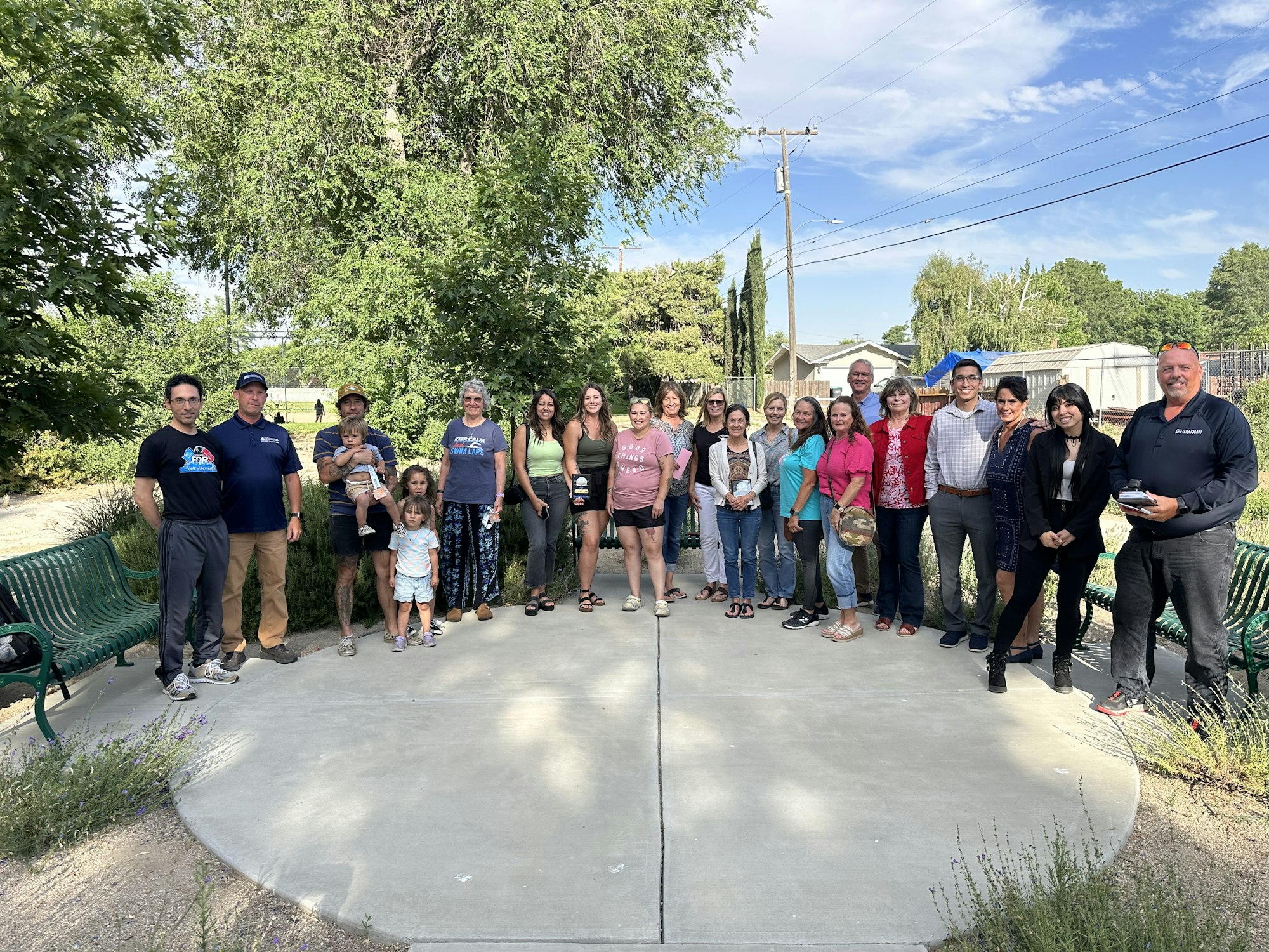 A group of people posing for a photo outdoors, with trees and a clear sky in the background.