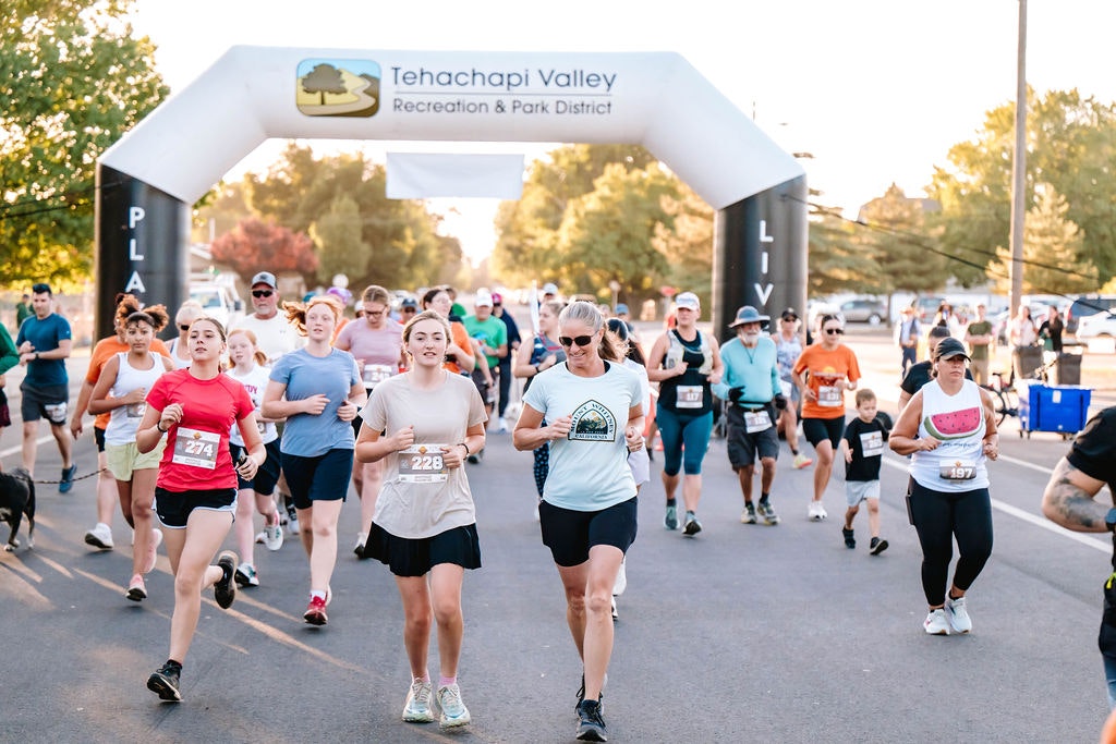 A group of people participating in a running event, passing under an inflatable arch labeled "Tehachapi Valley Recreation & Park District."