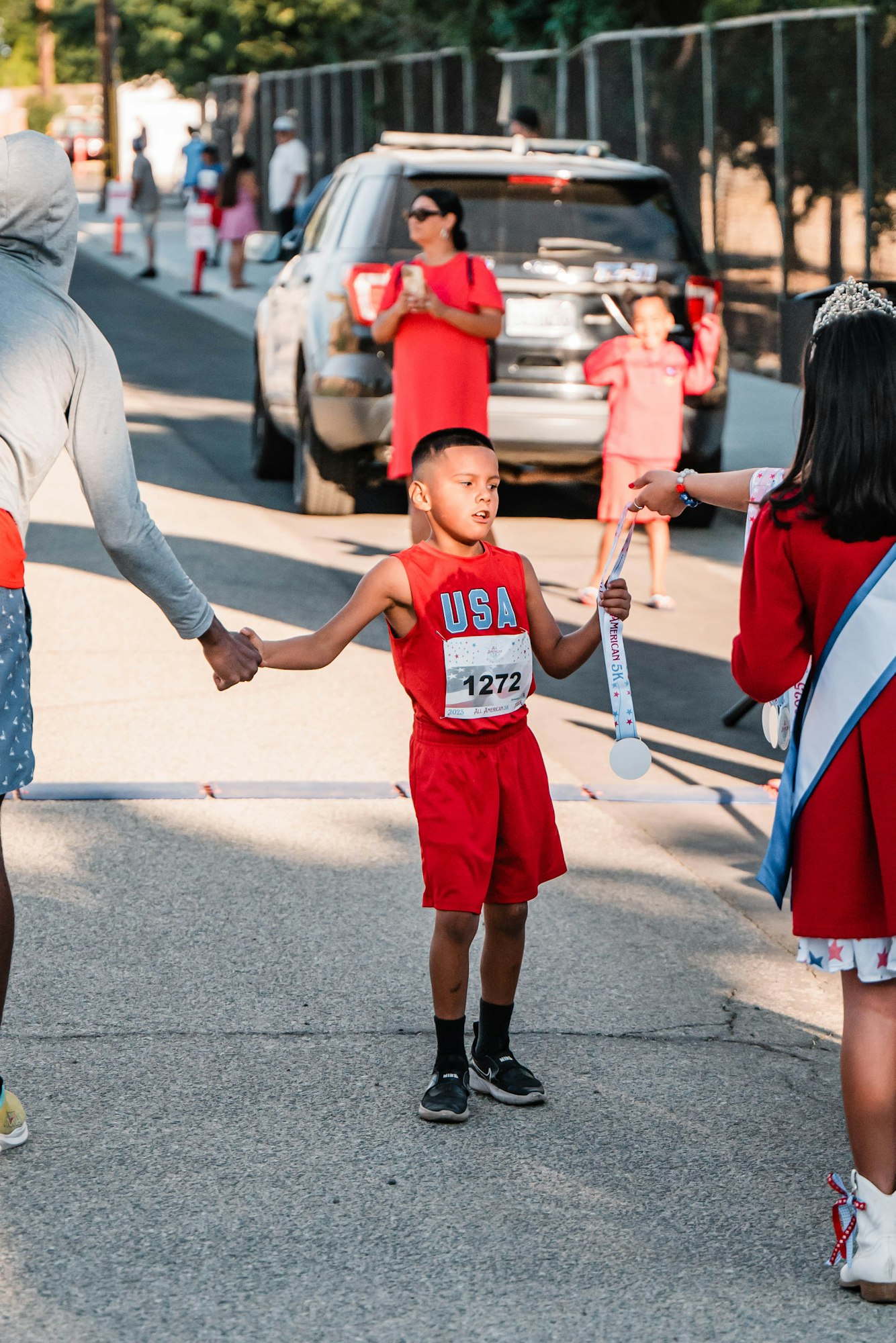 A young boy in a red "USA" outfit crosses a finish line and receives a medal.