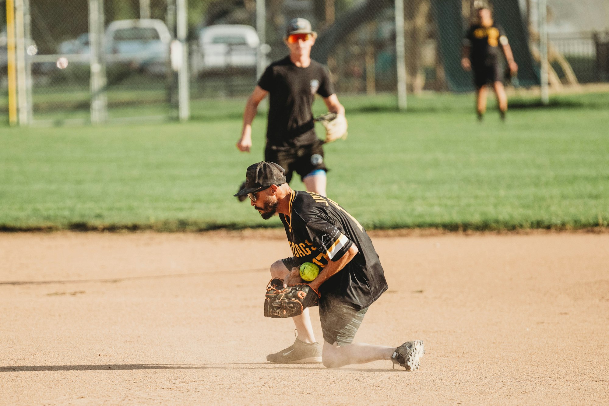 Baseball players on a diamond, one sliding into base, another in the background. Dust is kicked up, game in action.