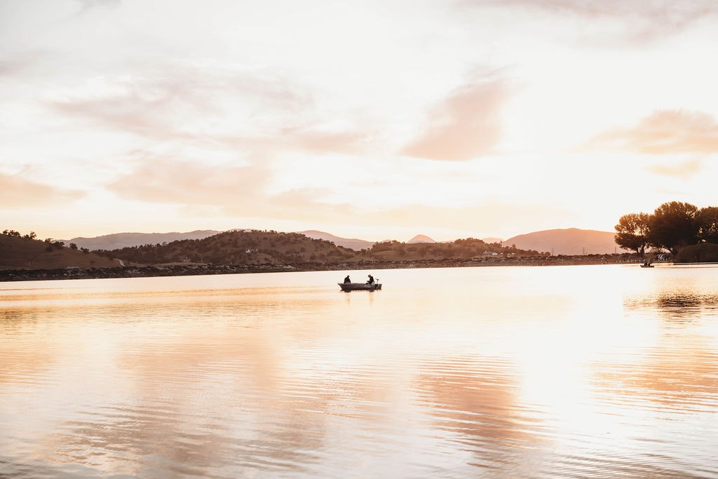 Sunset over a tranquil lake with hills in the background and a boat centrally placed on the water.
