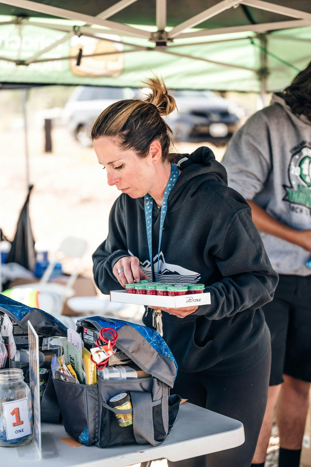 A woman organizing items on a table under a canopy, with a bag and other various objects around.