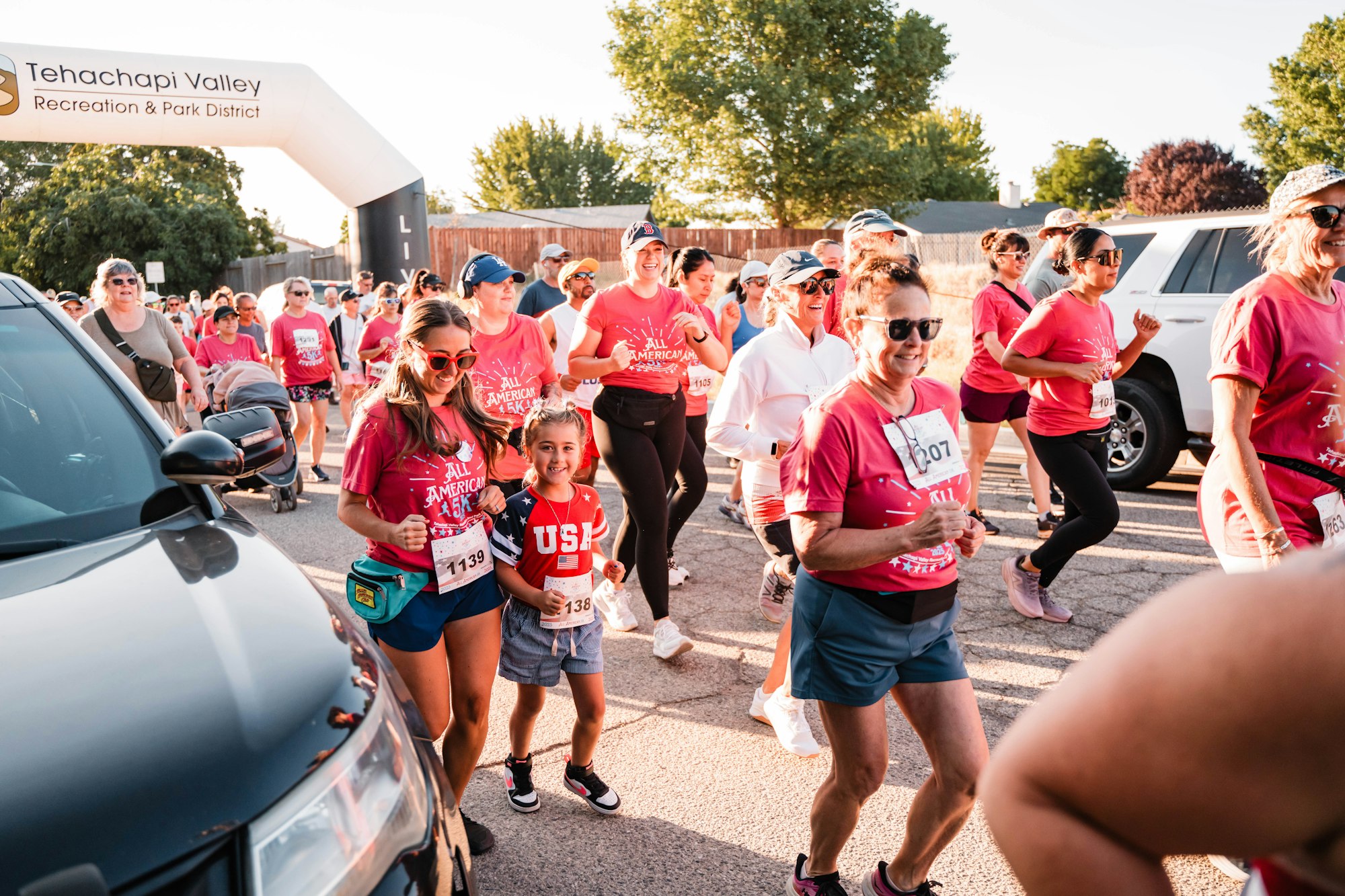 People participating in a community run, wearing red shirts and race bibs, under a Tehachapi Valley Recreation & Park District banner.