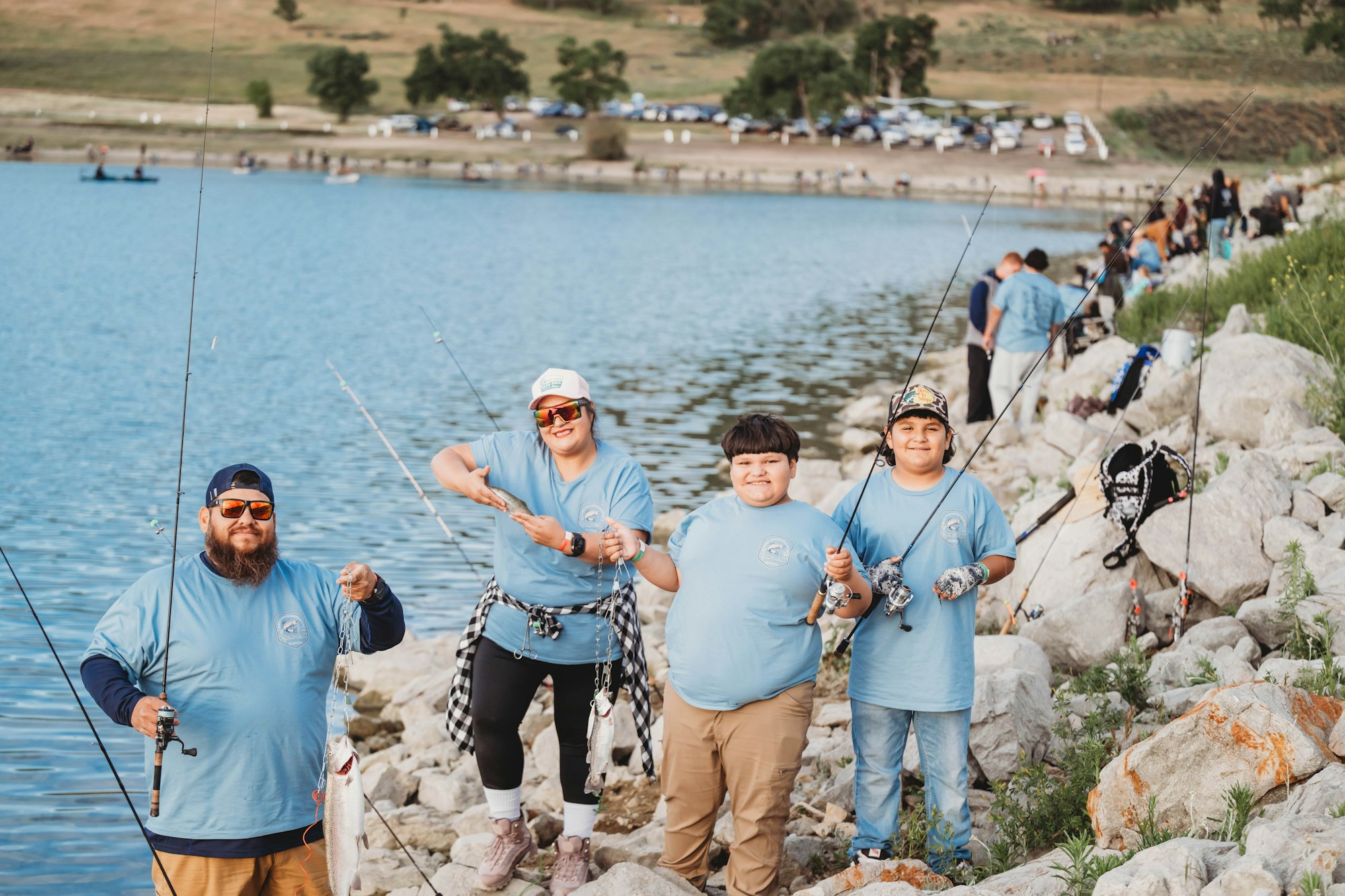 A group of people fishing by a lake, wearing matching blue shirts, with fish and fishing rods.
