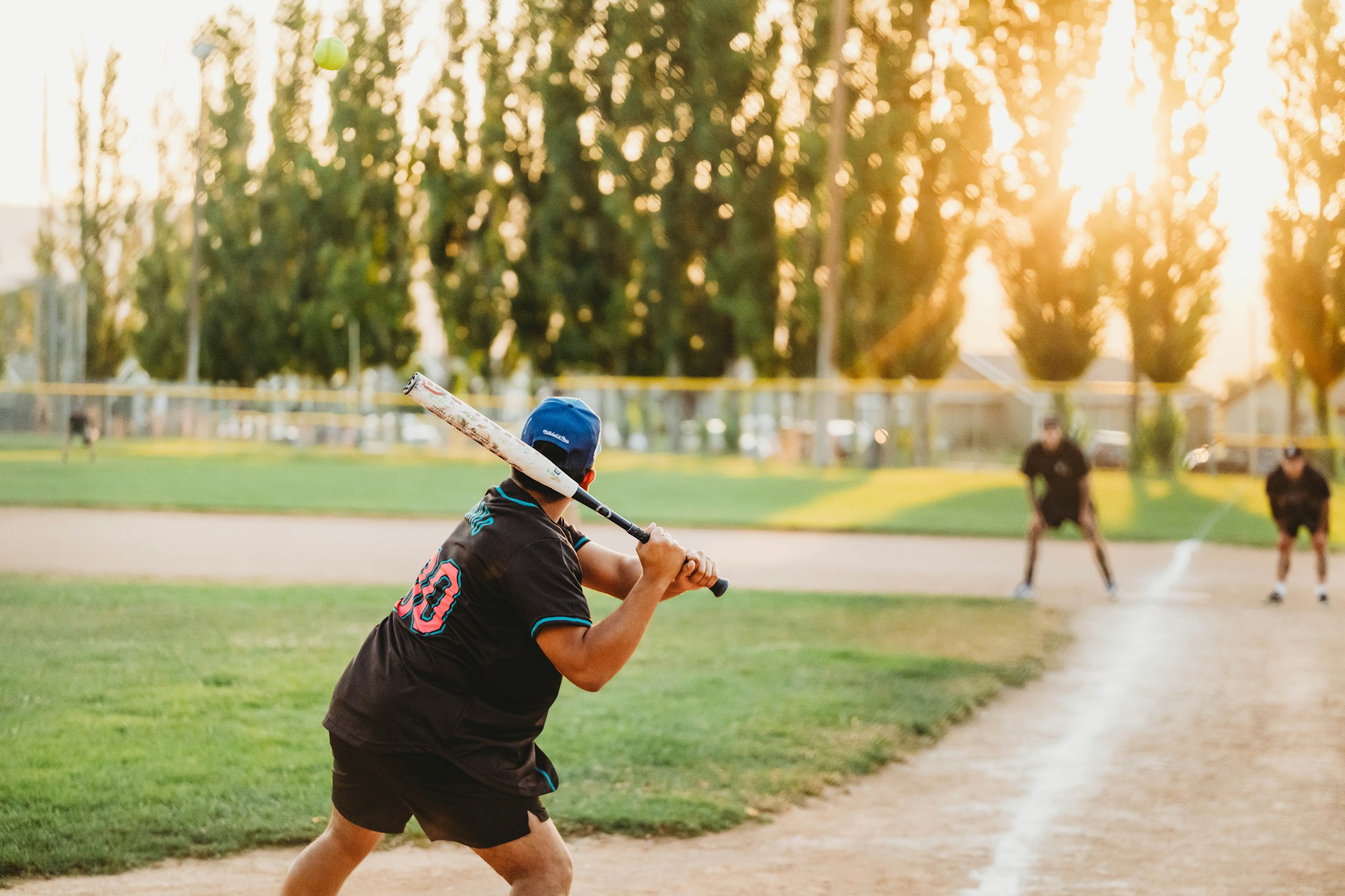 A person swinging a baseball bat with a sunset backdrop.