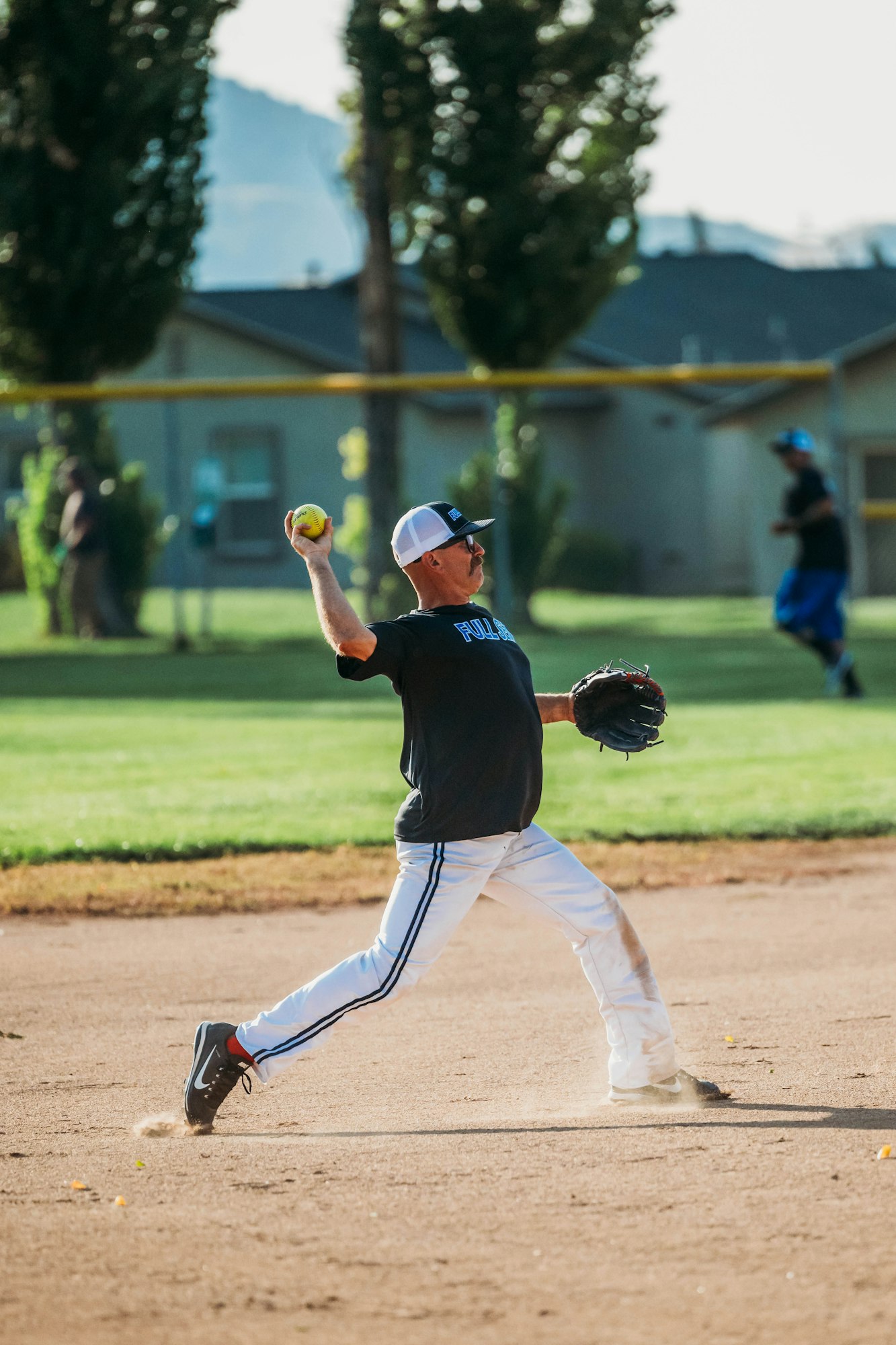 A softball pitcher mid-throw on a sunny day, focused and dynamic.