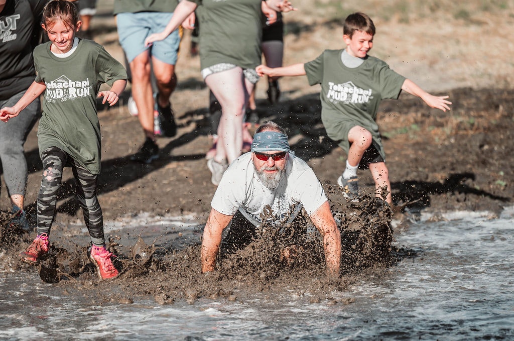 People participating in a mud run, splashing through a muddy water obstacle course.
