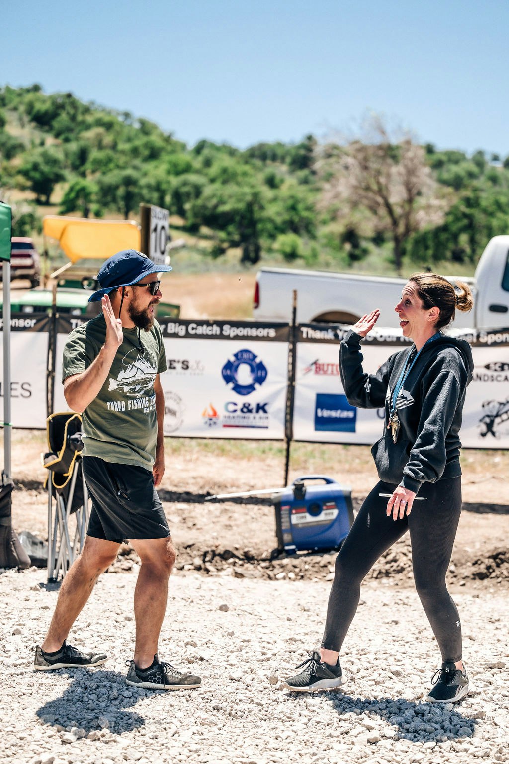 Two people seemingly engaged in an animated conversation outdoors, with sponsorship banners in the background.