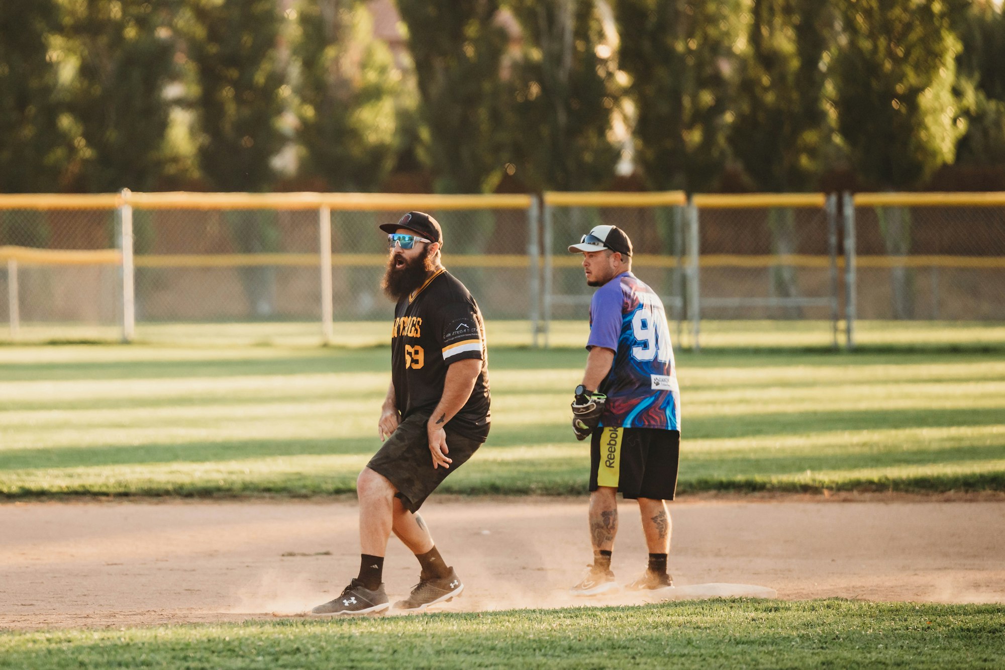 Two men playing softball, one fielding and one running bases, on a sunny field.