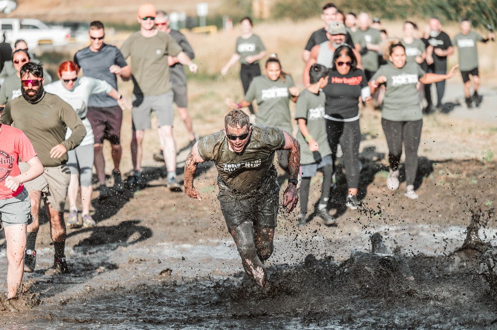 People running through mud at an outdoor obstacle course event.