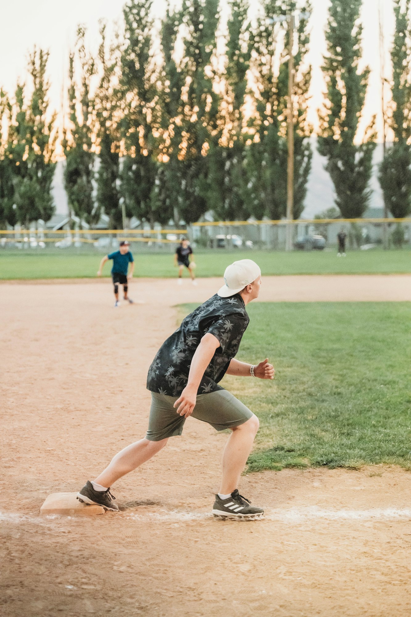A person playing baseball, running bases, with others in the background during dusk.