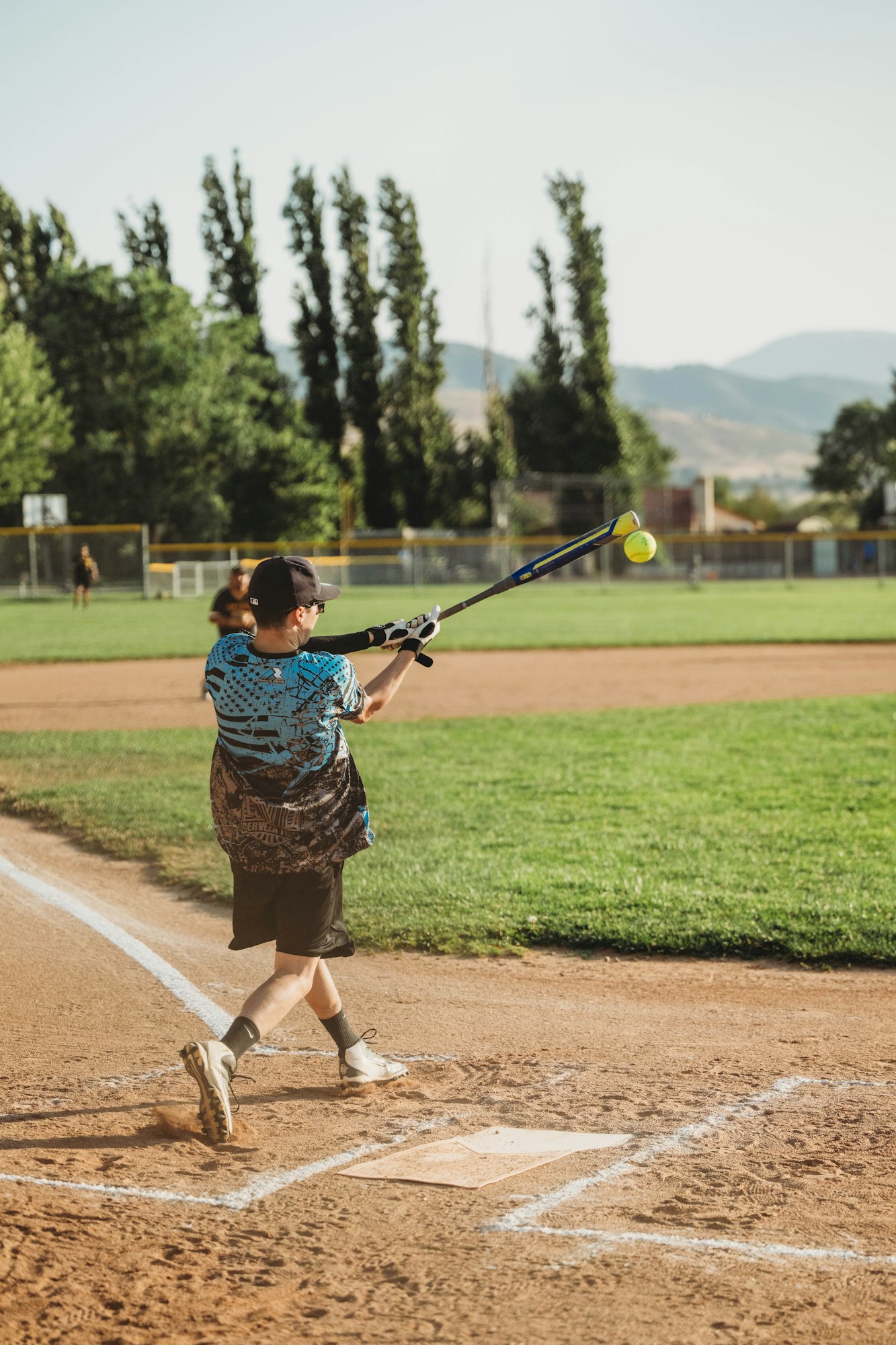 A person swinging a bat at a softball on a sunny day at the ballpark.
