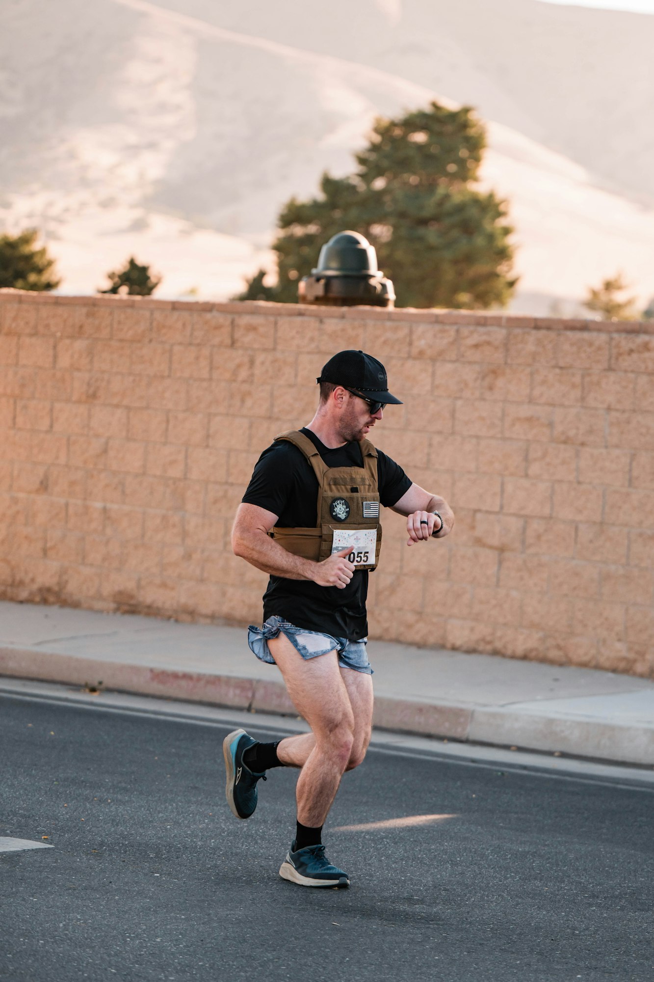 A person running on a street, wearing a weighted vest, shorts, cap, and checking a smartwatch.