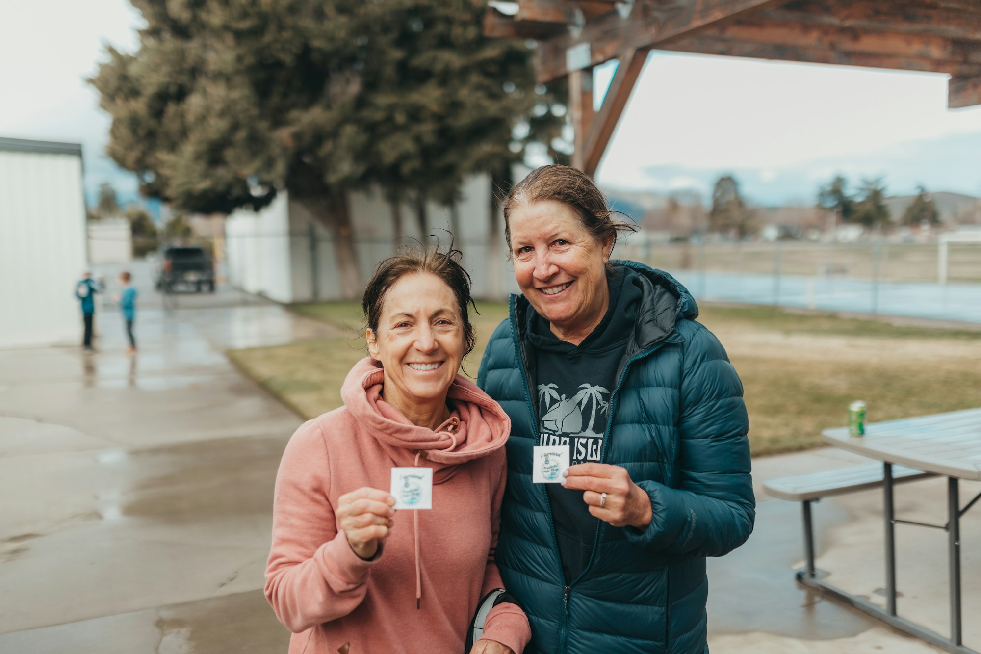 Two smiling women holding small cards outdoors.