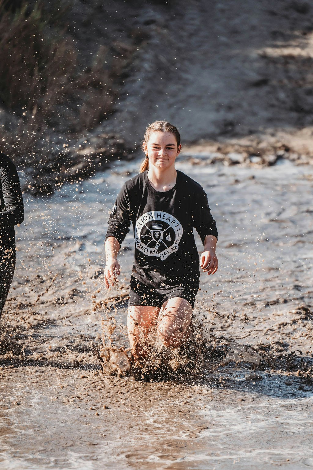 Person running through muddy water, smiling, wearing a black shirt.