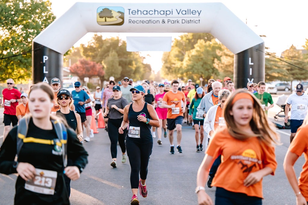 People running in a race under a "Tehachapi Valley Recreation & Park District" arch.