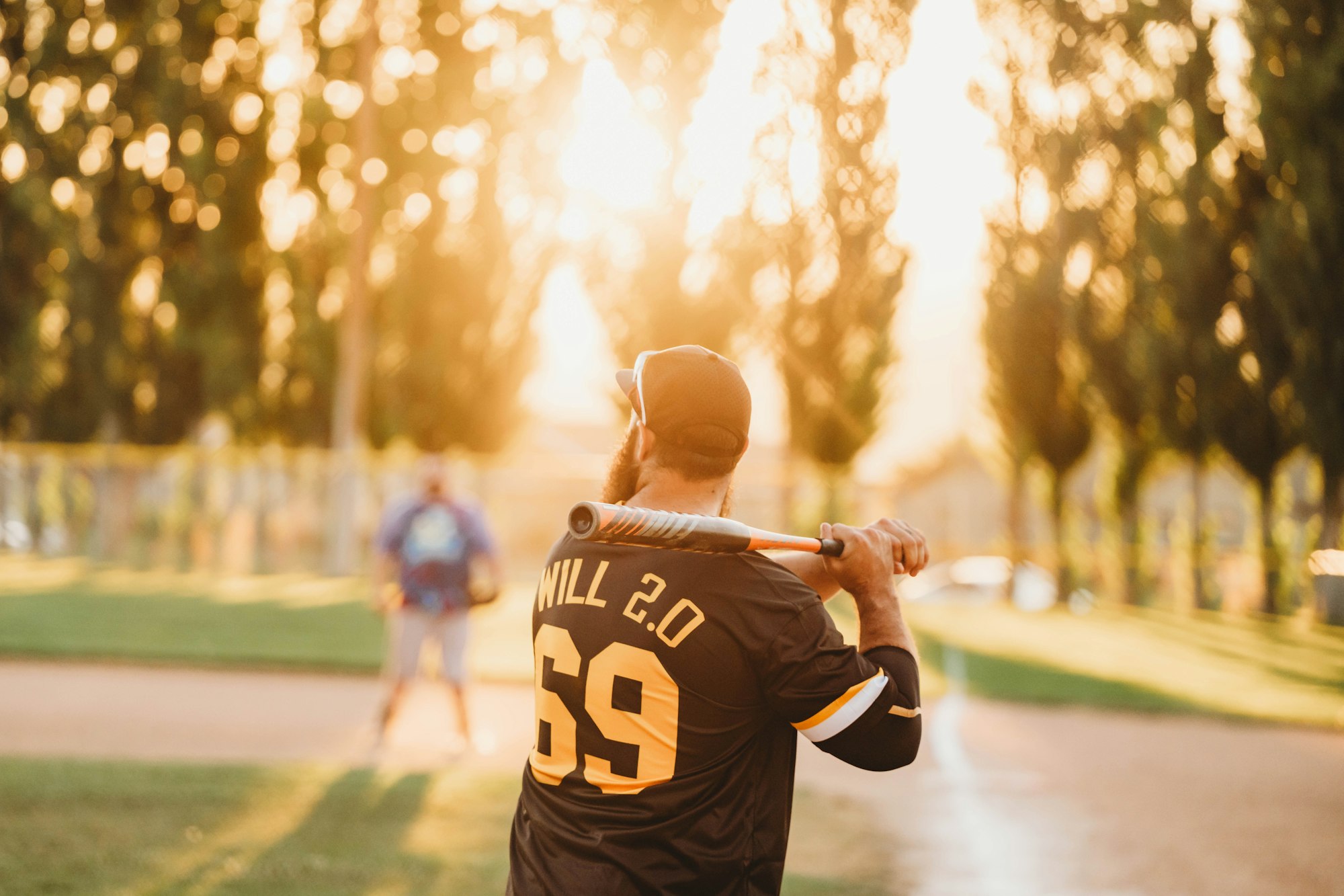 Person playing baseball at sunset with trees in the background.