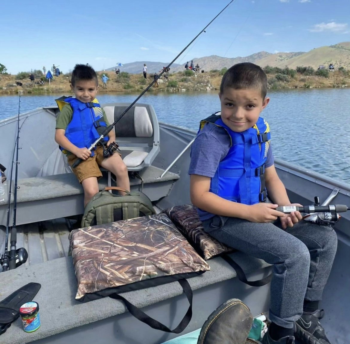 Two kids in life vests are fishing on a boat.