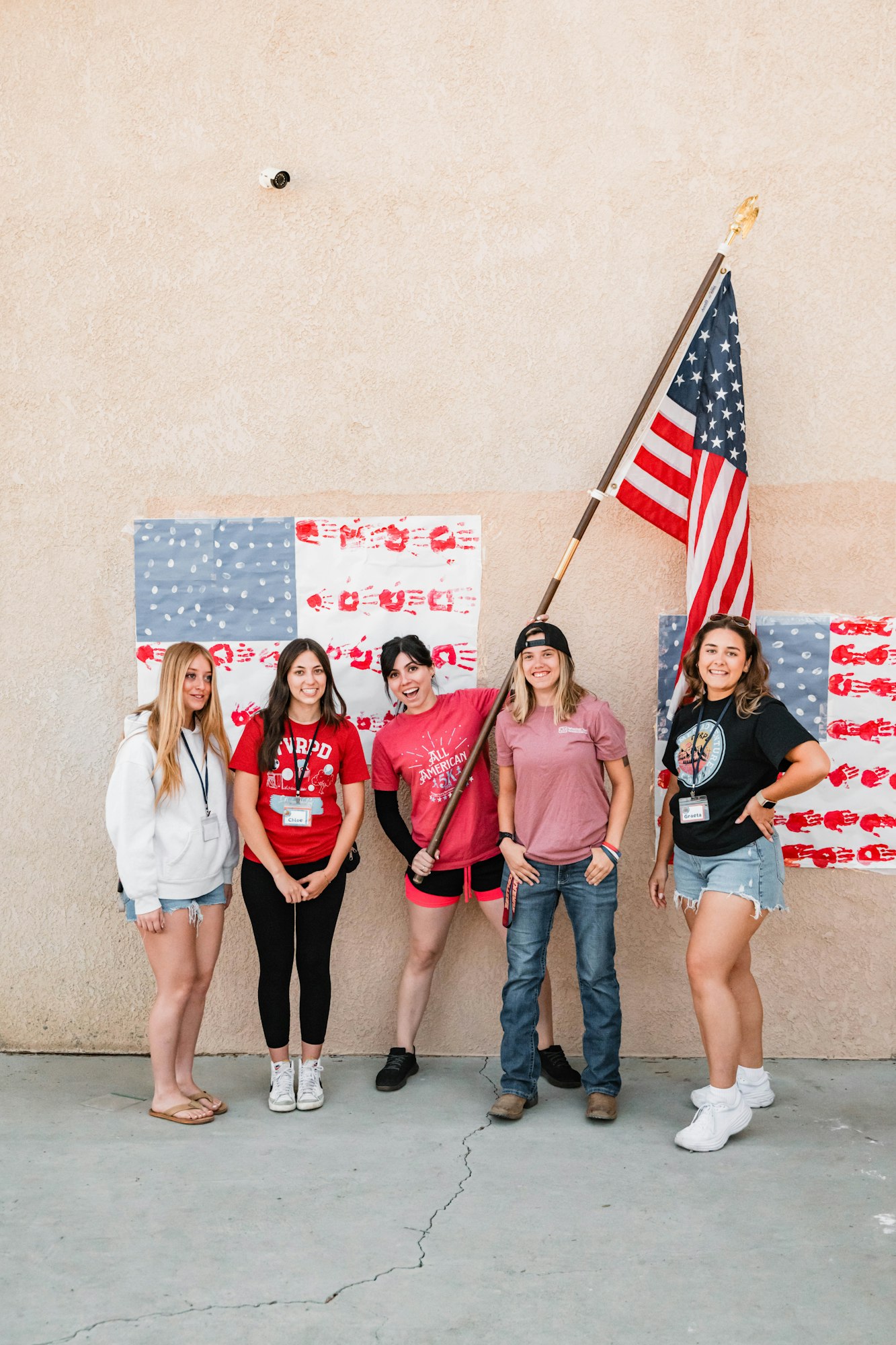 Five people posing with a USA flag and hand-painted flag art on a wall.