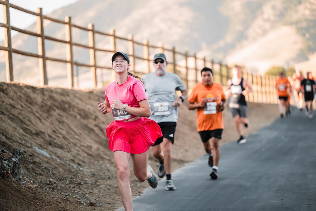 Runners participating in a race on a paved road with a wooden fence and mountainous background.