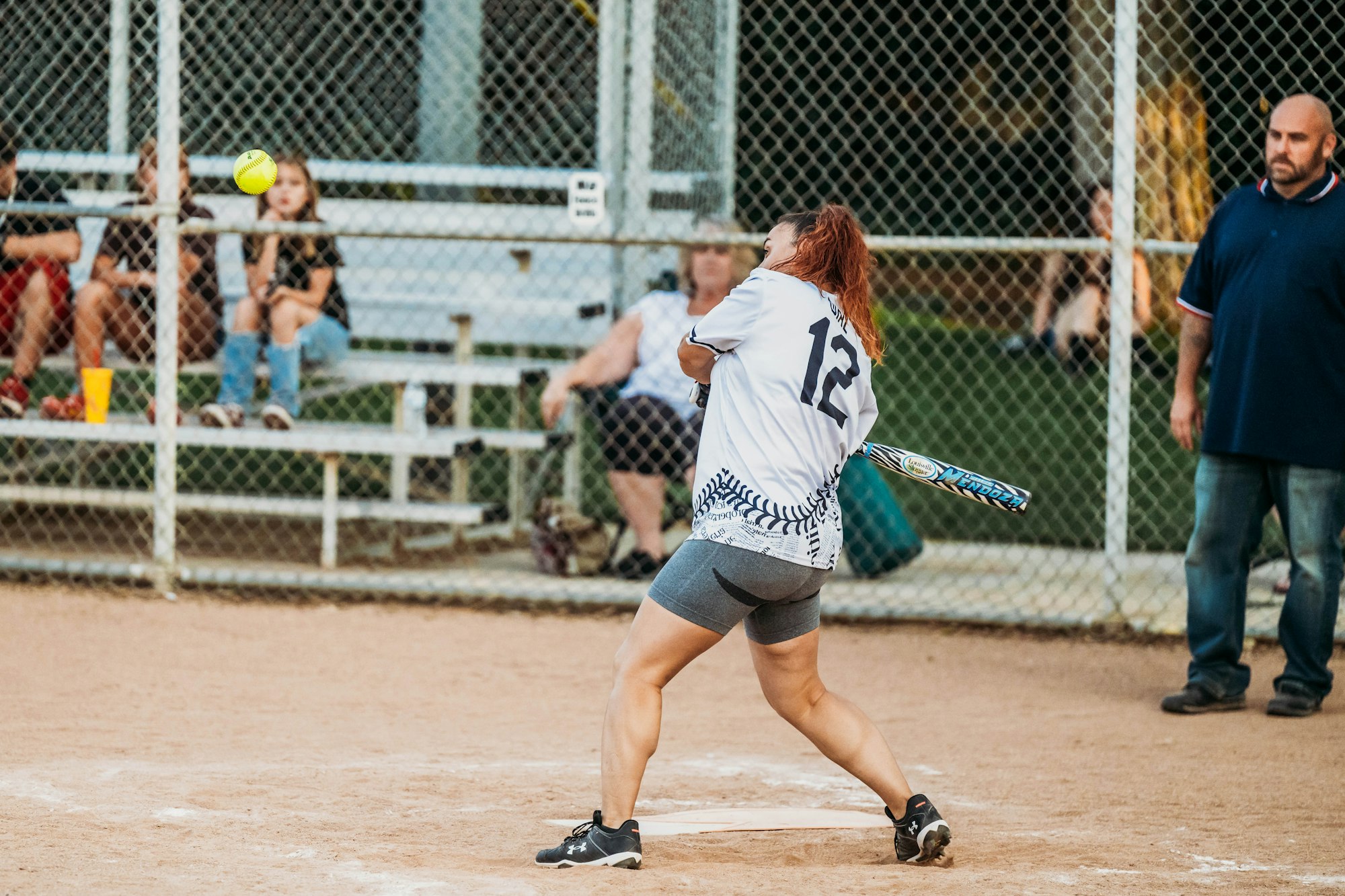 A softball player swinging at a pitch with spectators in the background.