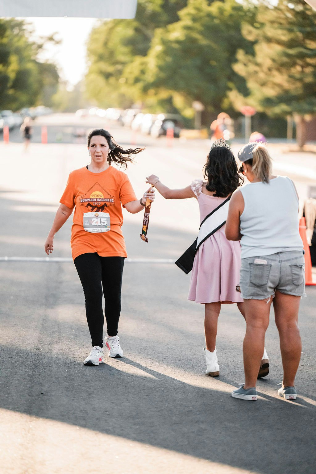 A runner receives a medal from a person in a sash and tiara.
