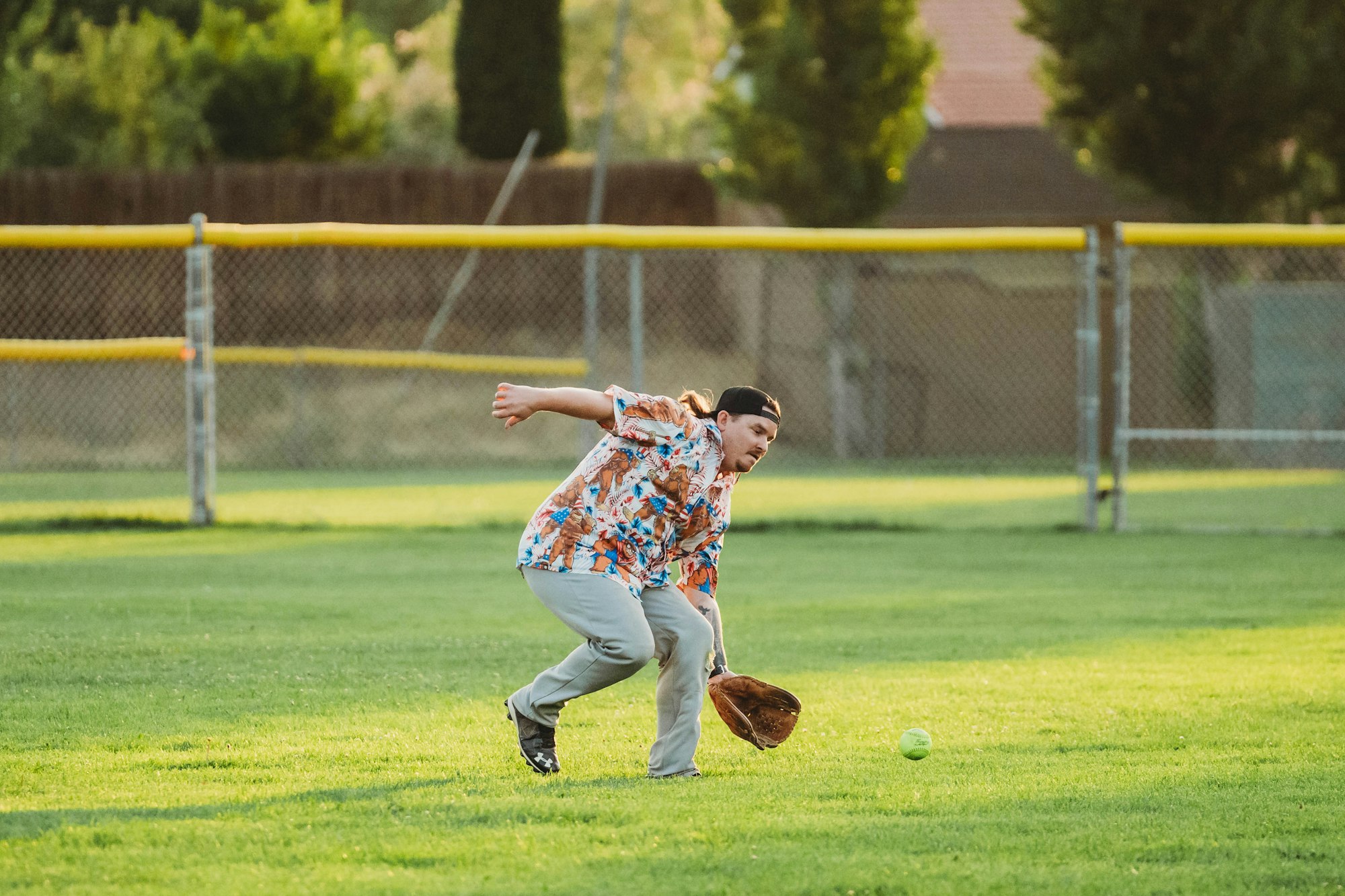 A person playing softball, missing a catch, in a colorful shirt on a sunny field.