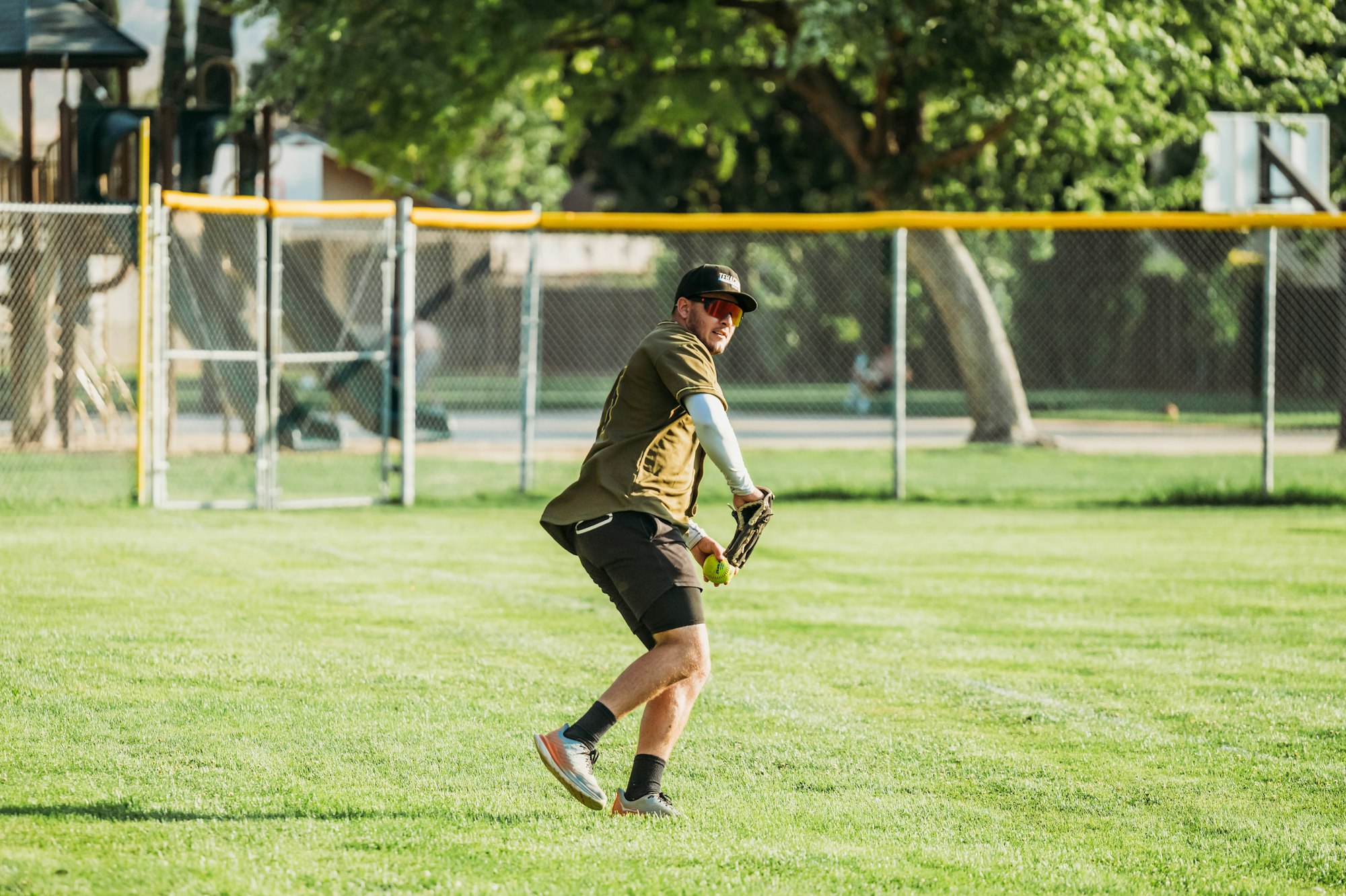 A person playing softball in a park, ready to catch a ball.