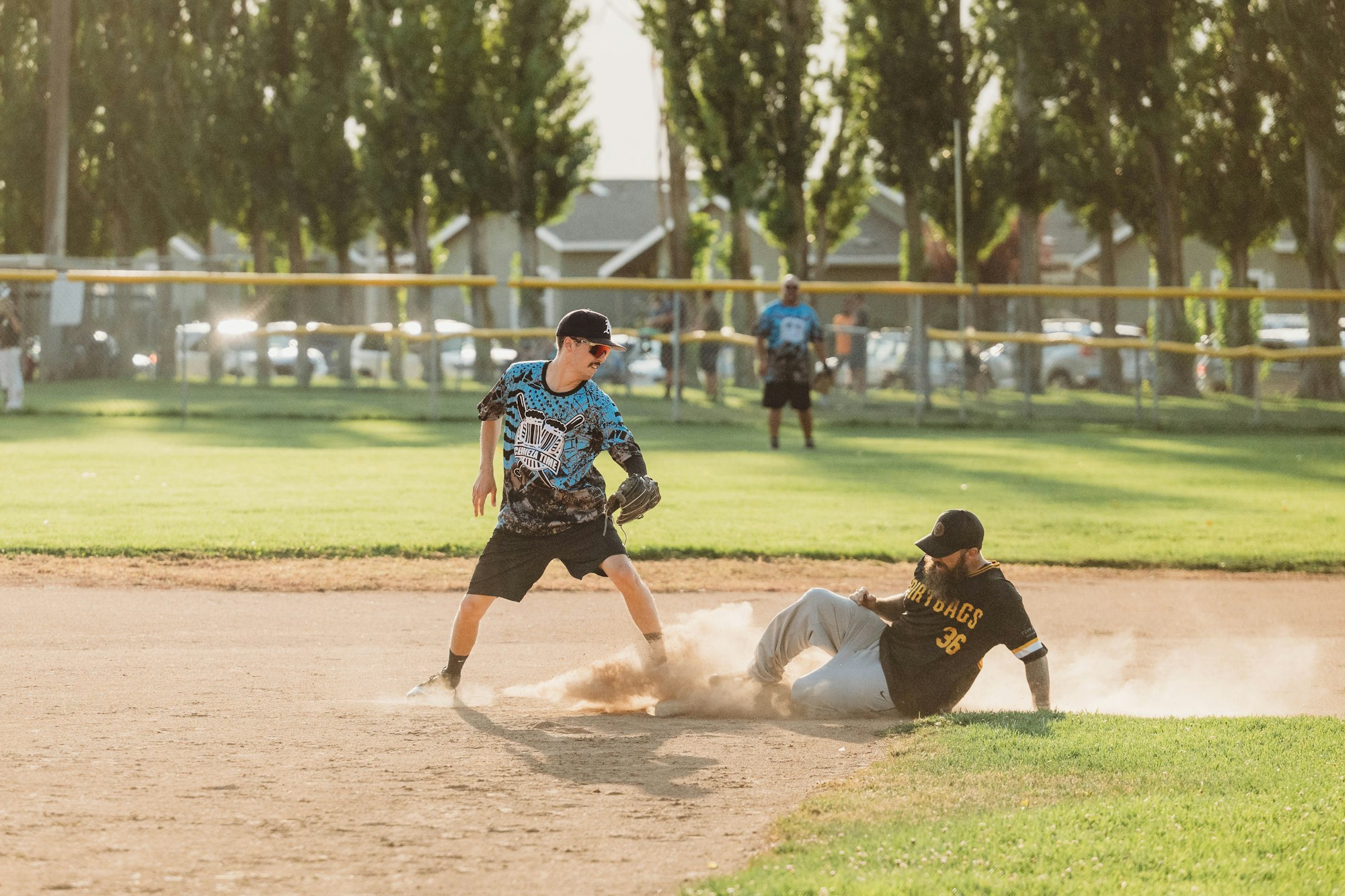Baseball players on a diamond, one sliding into base, another ready to tag. Dust, action, and sunlight.