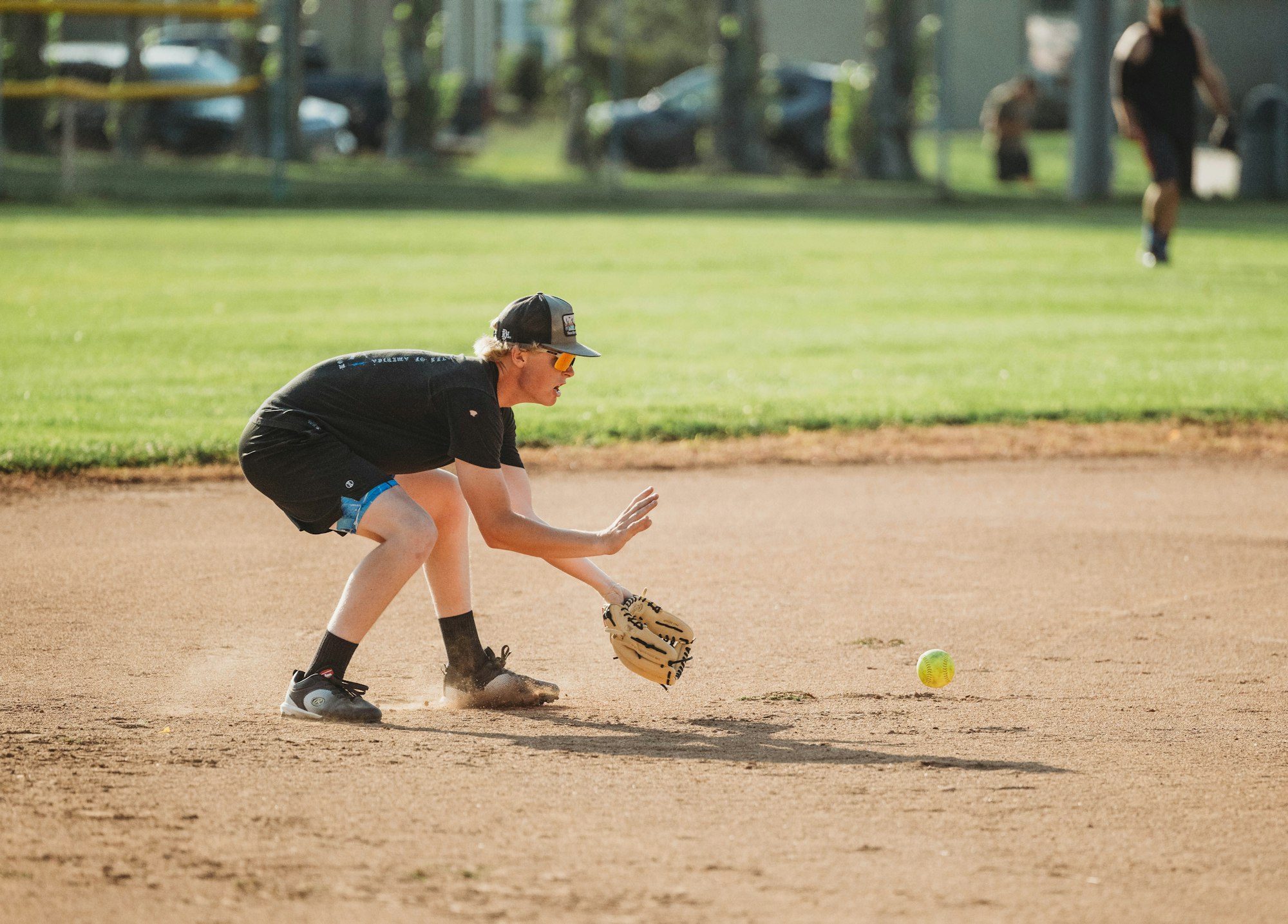 A person playing softball is ready to field a ball on a dusty infield.