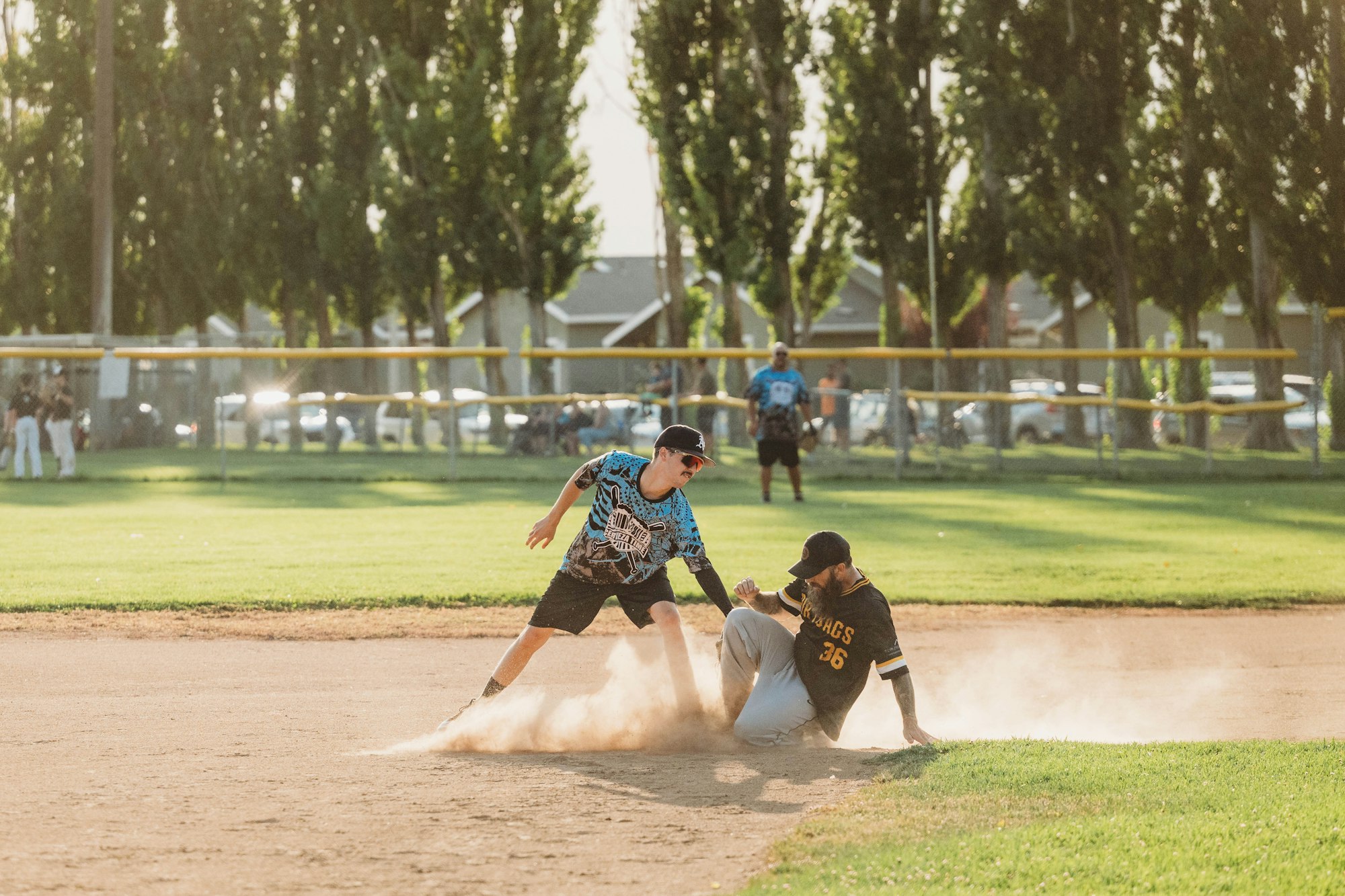 Two people playing baseball, one sliding into base and the other attempting to tag him out, on a sunny day.