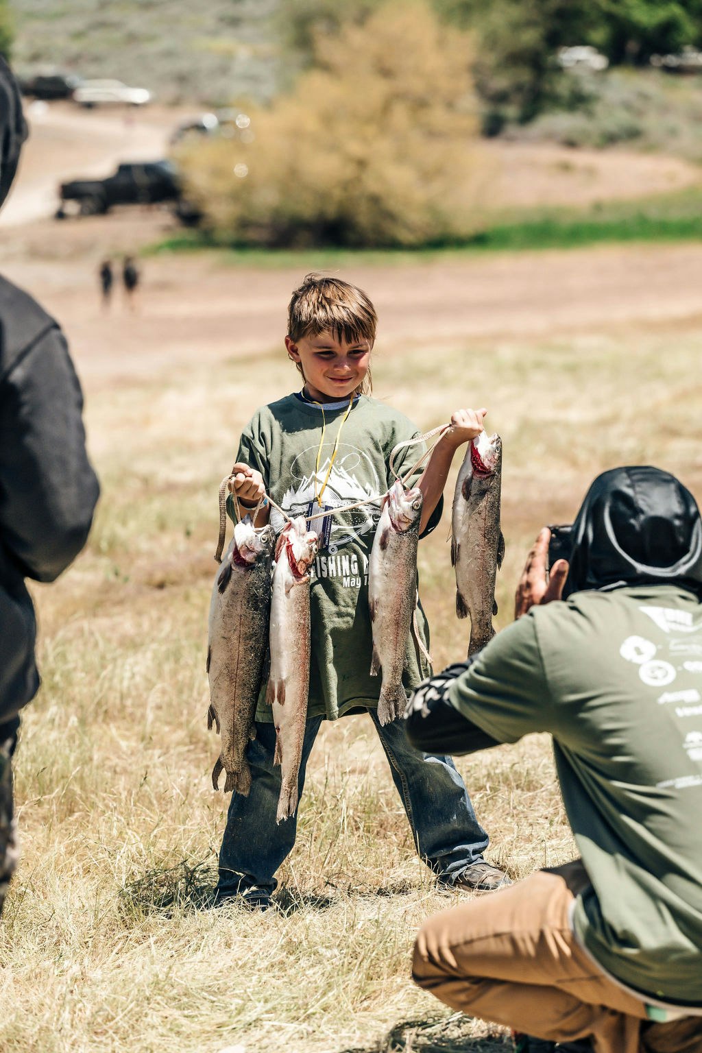 A child proudly holds a string of fish while being photographed outdoors.
